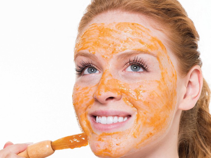 Girl with a brush puts a mask of carrots on her face