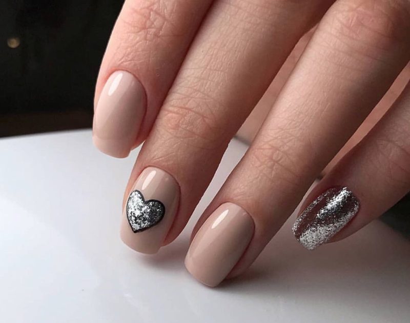 Unusual nude manicure with glitter and a silver heart.