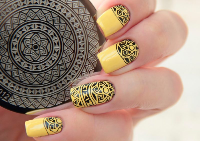 Yellow manicure with black ethnic stamp pattern.