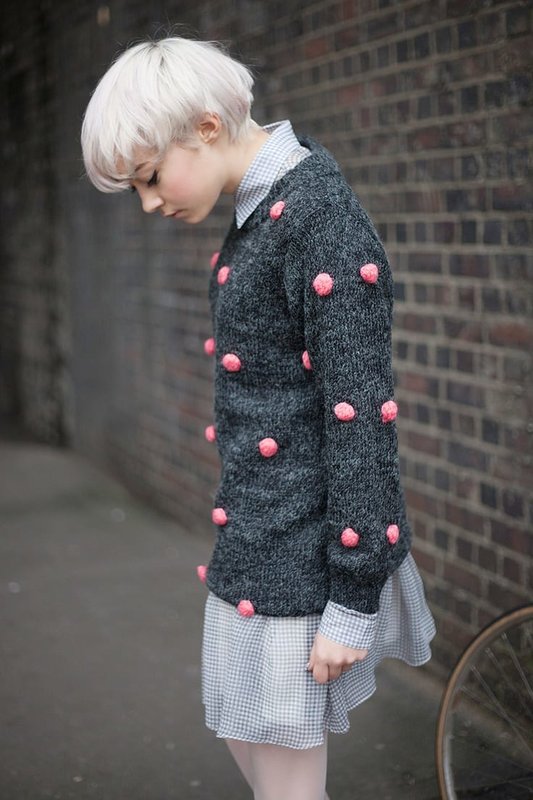 Girl in a sweater with pink pompoms over a dress