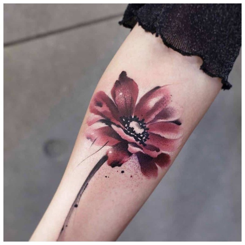 Watercolor tattoo in the form of a flower on the arm